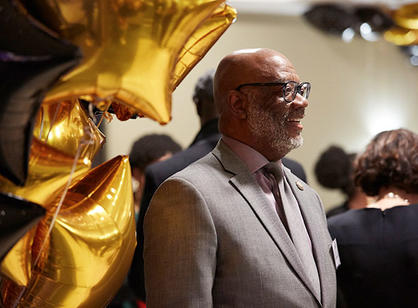 An alumnus stands in front of colorful balloons.