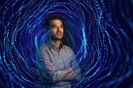 Male professor posing in front of blue background with arms folded.