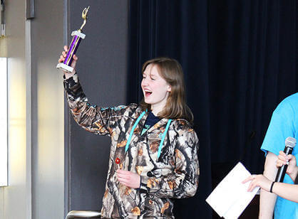 A high school student triumphantly raises her trophy