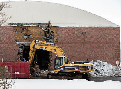 The side of the Field House with a large hole ripped into it, flanked by construction equipment