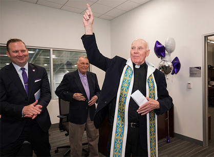 Rev. Earle Markey, S.J. '53 (left), blesses the office of the athletic director in honor of Ron Perry '54, with Nate Pine (right), the College's current athletic director.