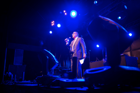 The College president stands on a dark stage speaking into a microphone.