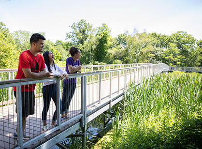 Three students stand on a bridge outside and laugh