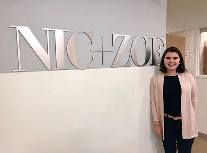 A student stands in front of the sign for NIC + ZOE