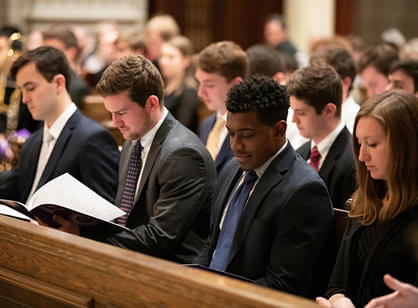 A group of students sit in the pews of St. Joseph Memorial Chapel