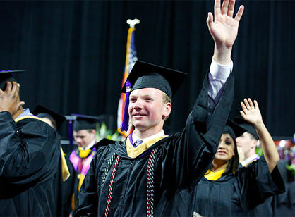 A student waves while processing into the DCU Center.