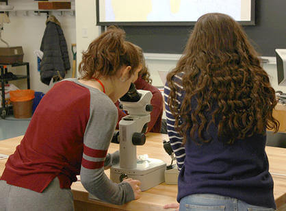 Two high school students look through a microscope during Women in Science Day
