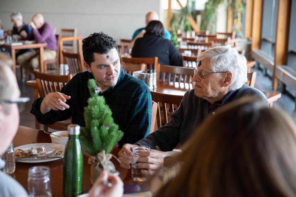 Young man sits with an older gentleman sit at a table looking at each other