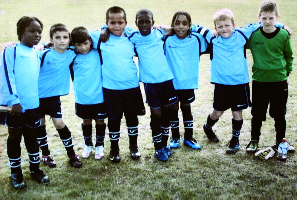Eight young boys stand with arms on each other's shoulders wearing soccer uniforms