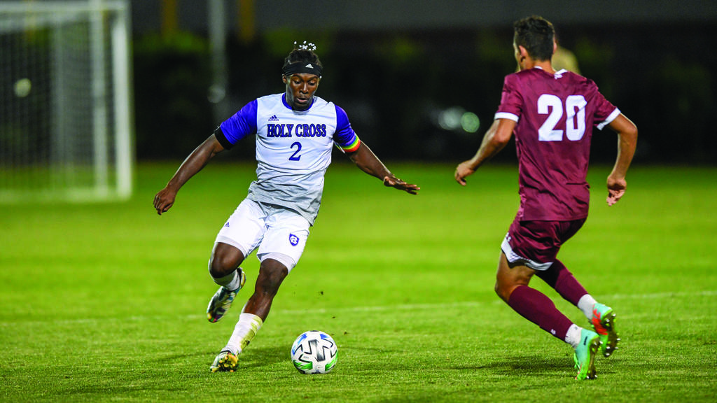 A soccer player in a white uniform with the ball tries to get passed a player