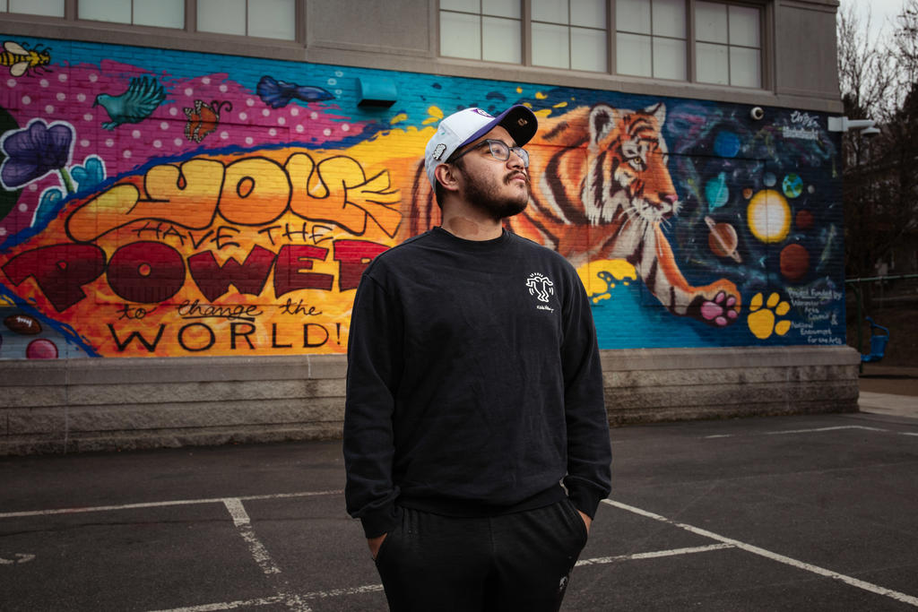 A man stands in front of a large mural, looking away from camera