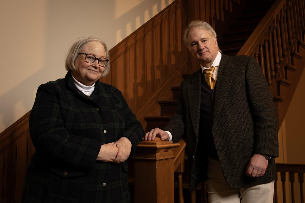 A man and a power in business attire lean on a wooden stairwell