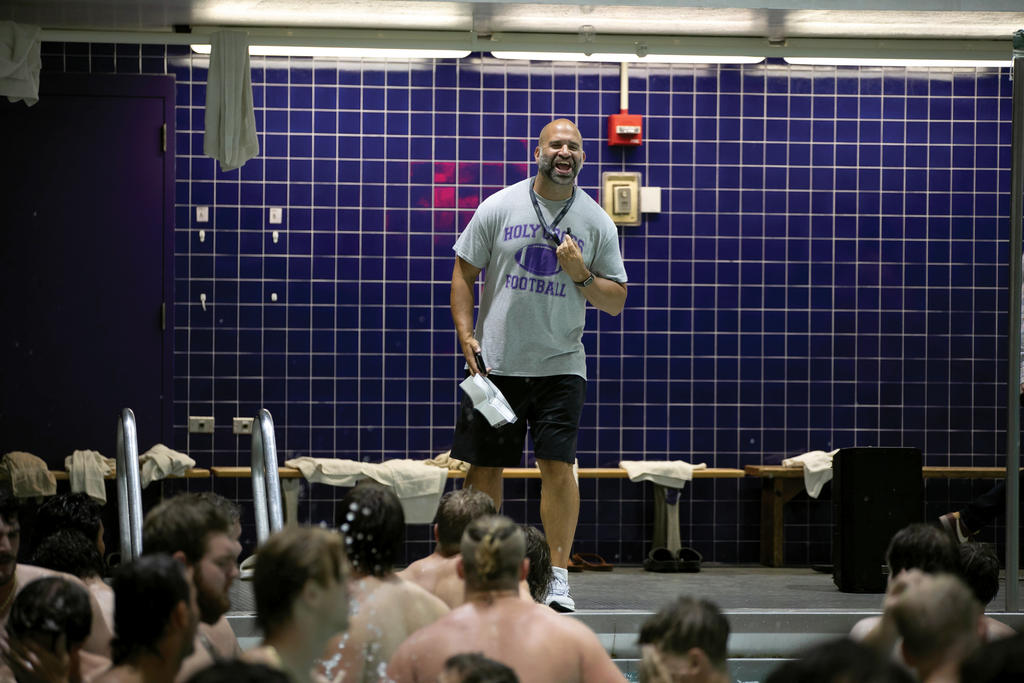 A man in t-shirt and shorts holds a whistle while standing on the edge of a pool