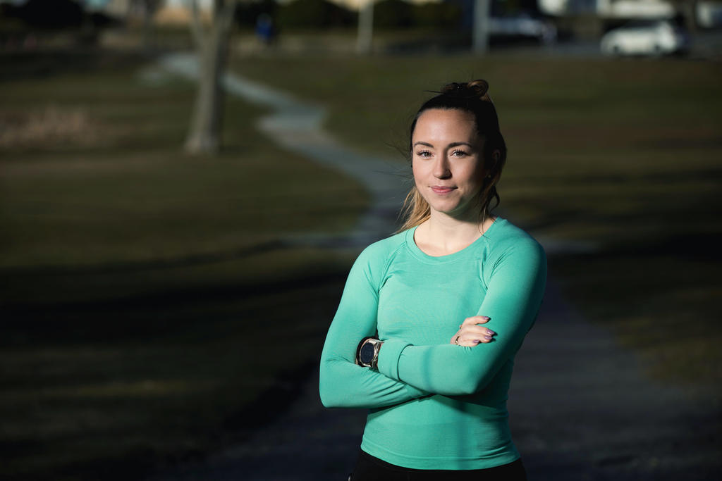 A woman runner with arms crossed smiles at camera