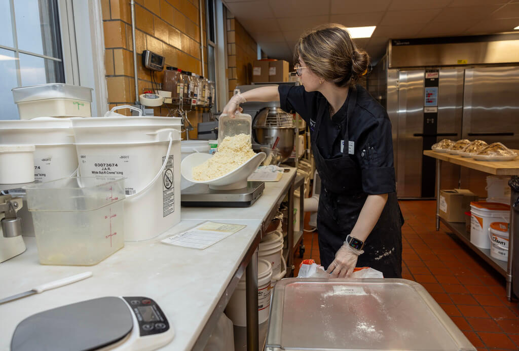 Bakery Assistant Samantha Lucier weighs recipe ingredients before combining them in the industrial mixer.