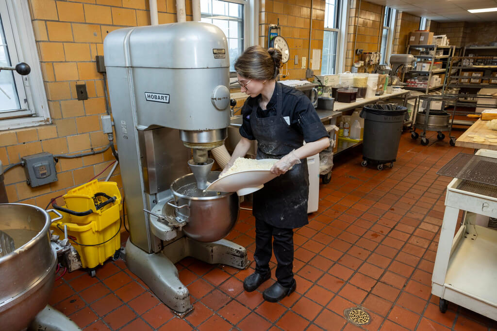 Women adds baking ingredients to large mixer