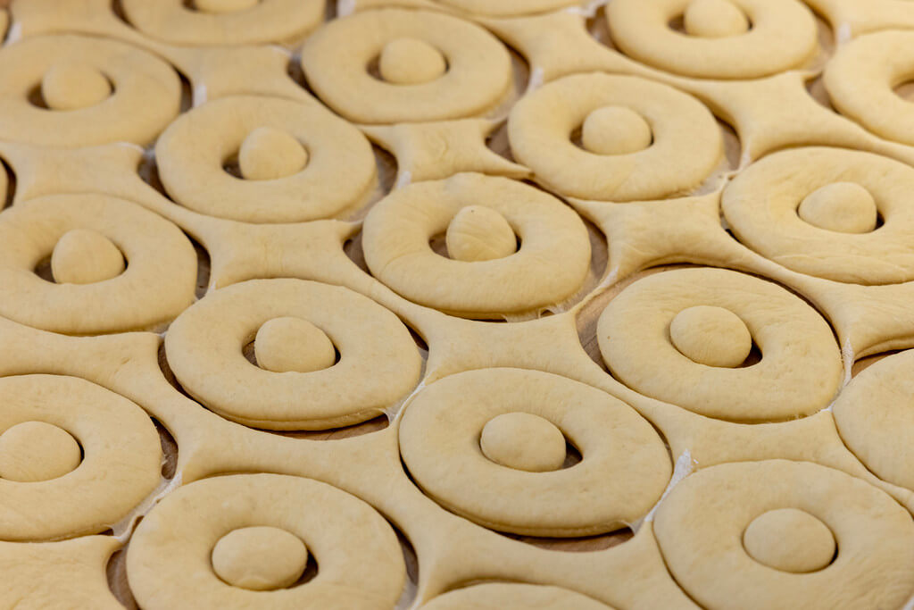 Donut holes are harder to flip in the fryer, so they and the edges from the first press are used in a second press. This "second roll" comes out tougher and more elastic due to the gluten and are used for specialty donuts that are more cake-like.