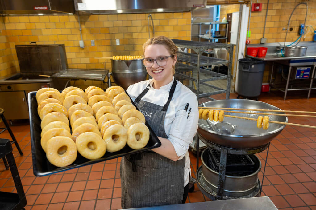 Woman holds tray of glazed donuts