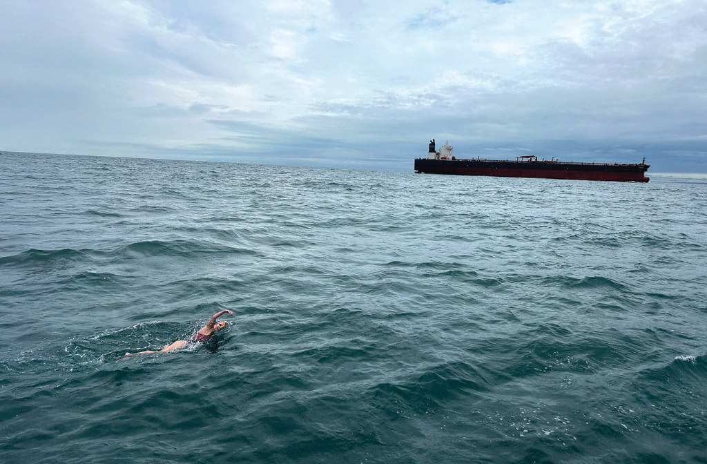 Swimmer in water with large boat in distance