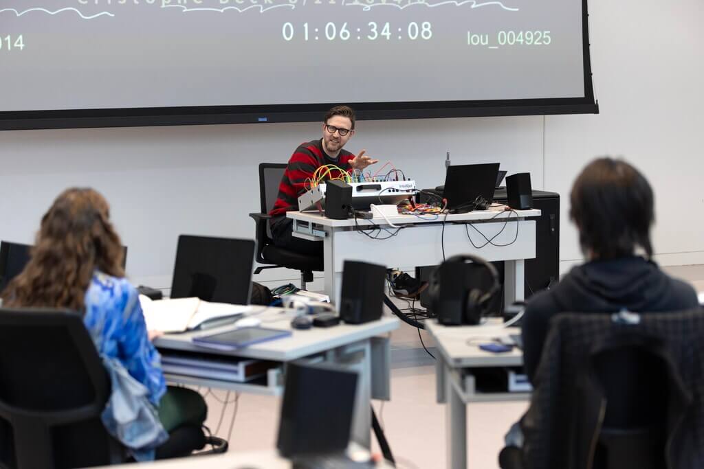 Man t desk talks to seated students