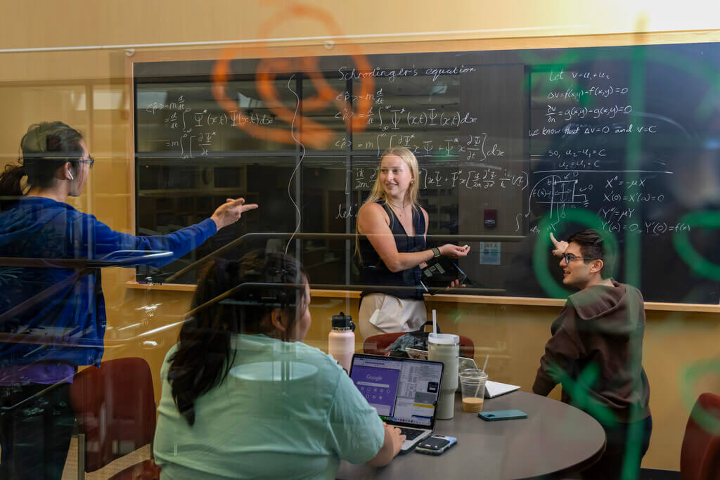 Student at a chalkboard talking with other students