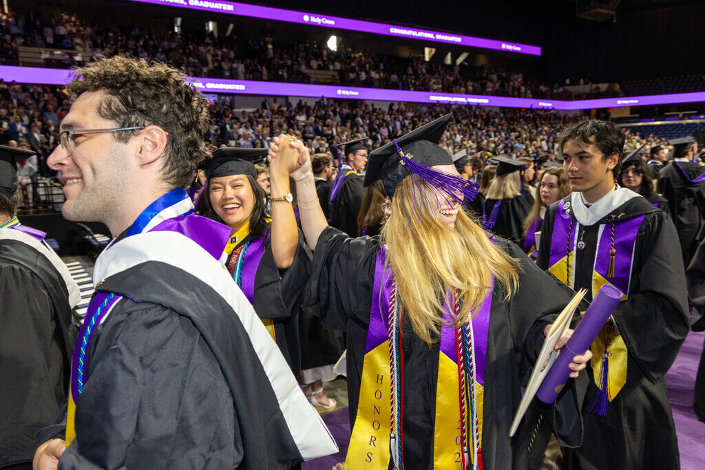 Graduates holding hands and cheering after receiving degrees