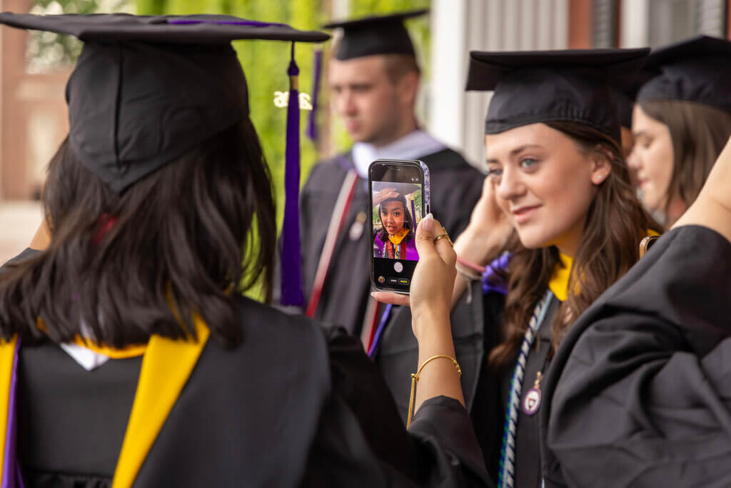 Graduate fixing her cap using her phone camera as a mirror