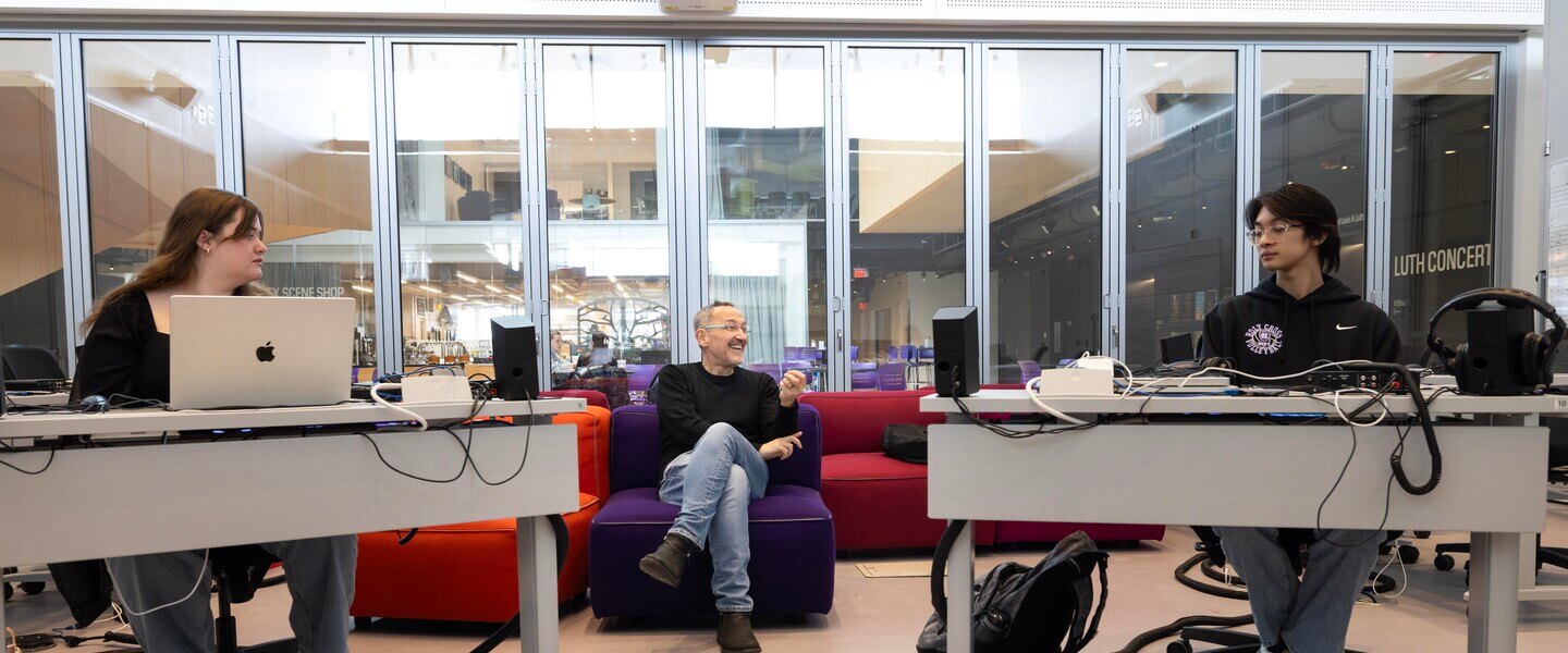 Man on couch in between two people at desks
