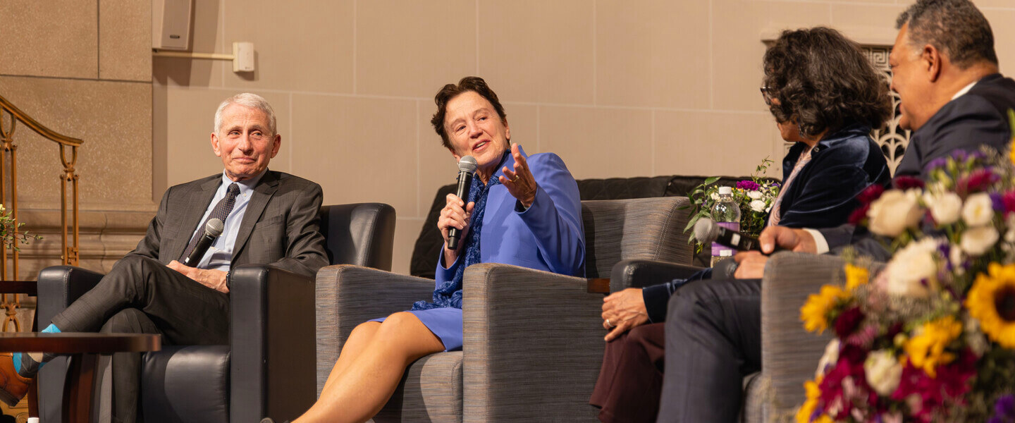 Seated woman speaks into microphone flanked by three other seated people