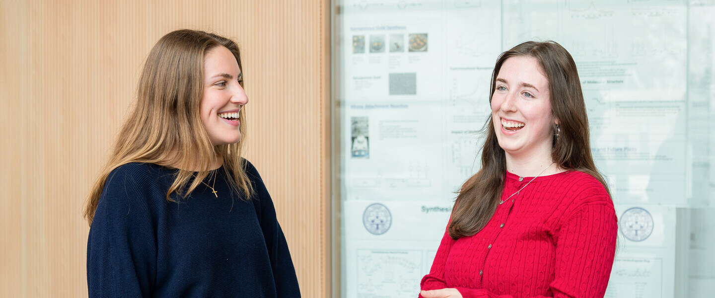 Two women in conversation in front of a whiteboard.