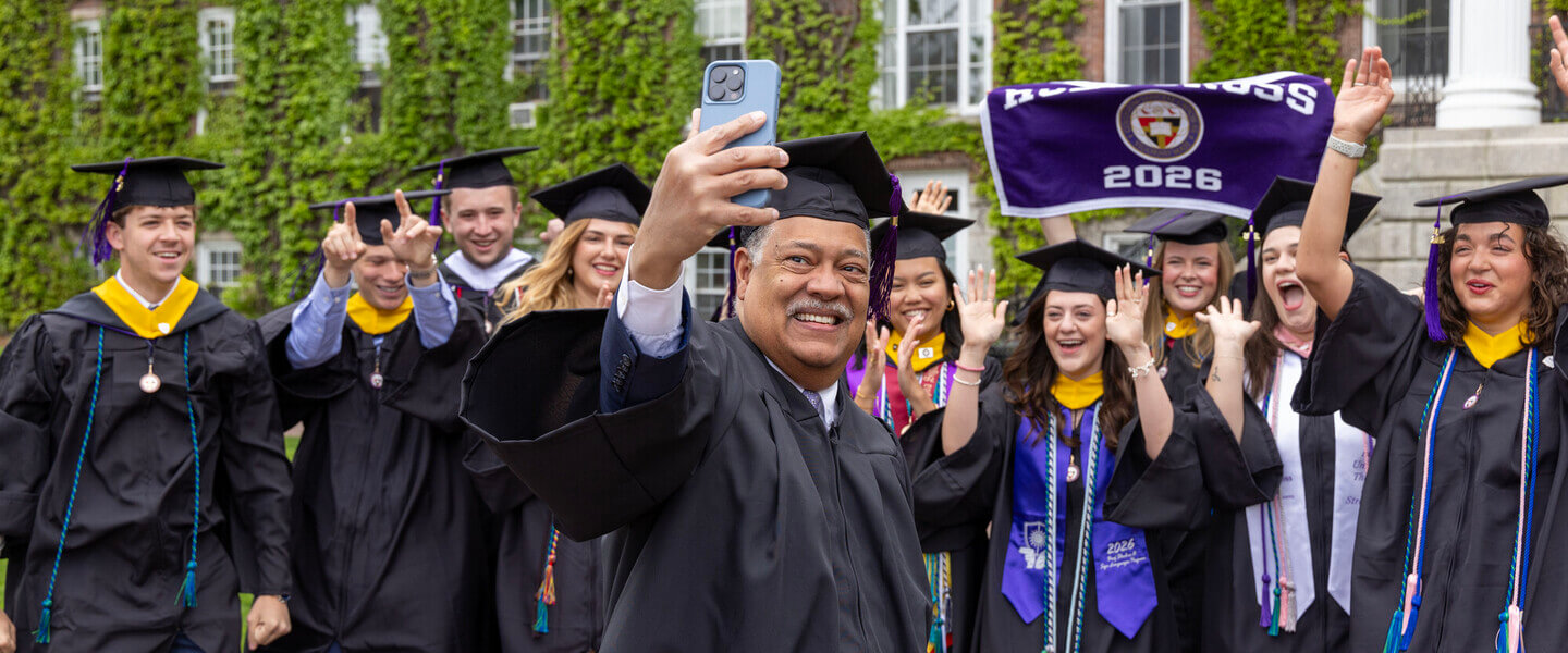President Rougeau taking a selfie with graduates in front of Fenwick Hall