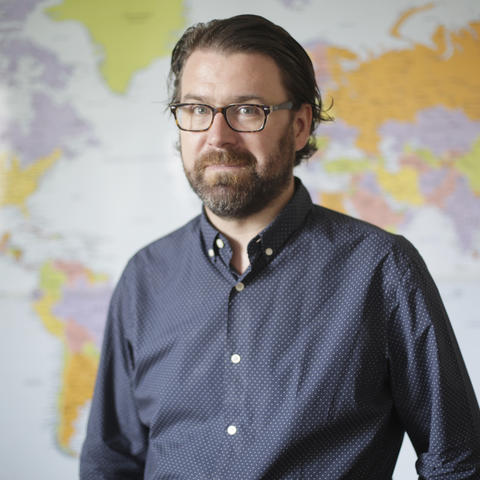 Holy Cross Professor Daniel Klinghard standing in front of a world map.