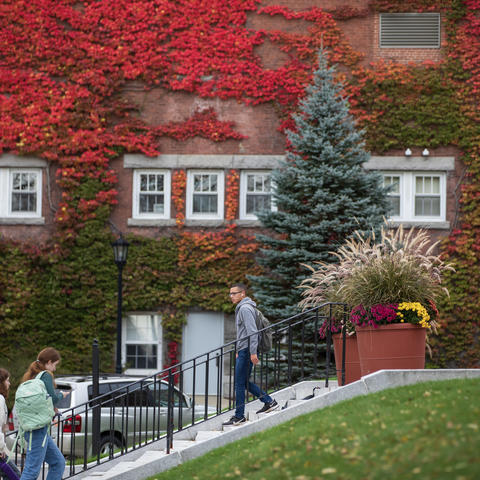 Red ivy covering a brick building. Students walking in front of the building