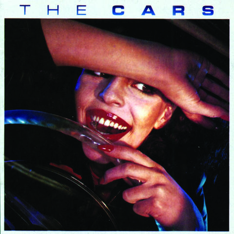 Album cover for "The Cars", a woman behind a steering wheel, with a hand on the wheel and her forearm on her head