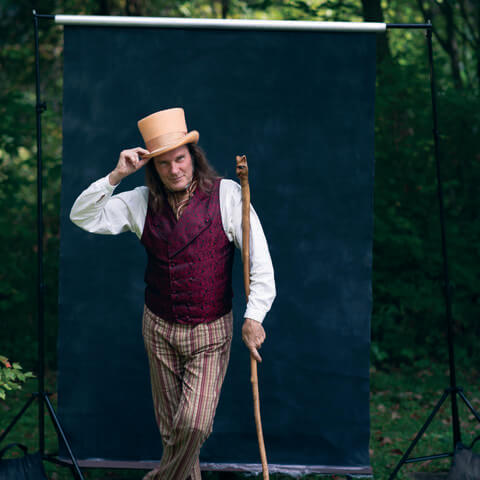 A man in a top hat, carrying a cane, poses in front of a photo backdrop