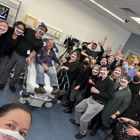 A group of men and women in a practice medical facility wearing clear masks posing for a picture.