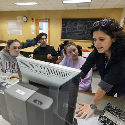 Female chemistry professor works with students at a computer in her lab.
