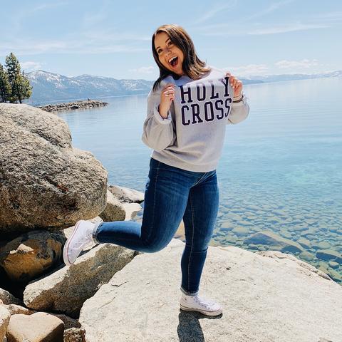 A young woman pulls at her Holy Cross sweatshirt with Lake Tahoe behind her