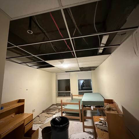 Ceiling tiles clutter the floor as a wires run across the bare ceiling