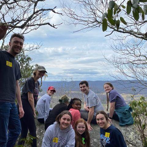 A group of college students pose for a photo at a valley overlook.