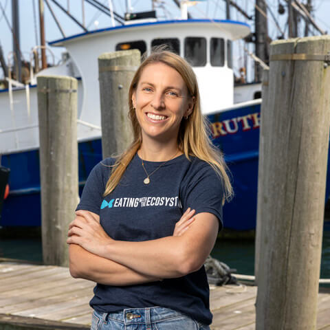 Woman in t-shirts stands on dock in front of a boat