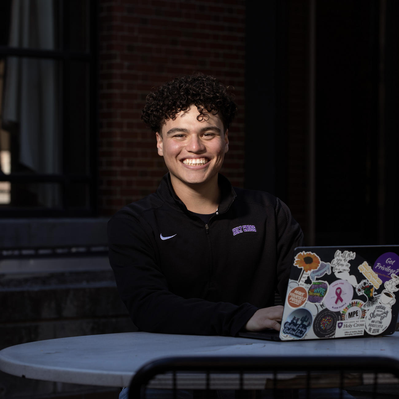 Young Hispanic male student sitting at a table with a laptop.