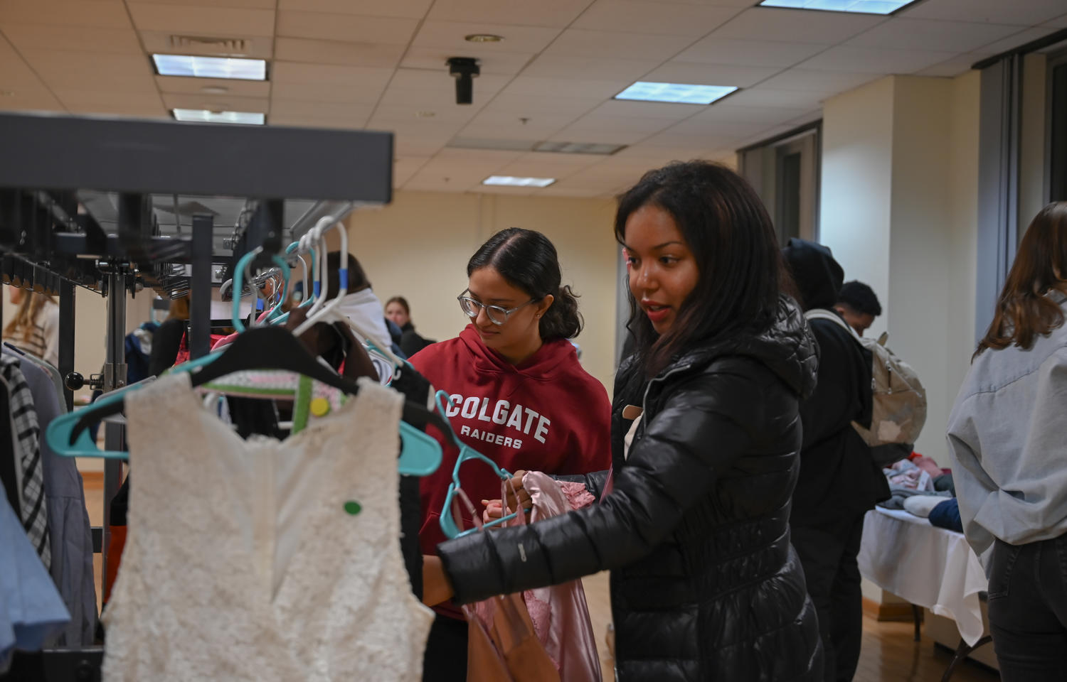 Young women look through thrift store clothing racks.