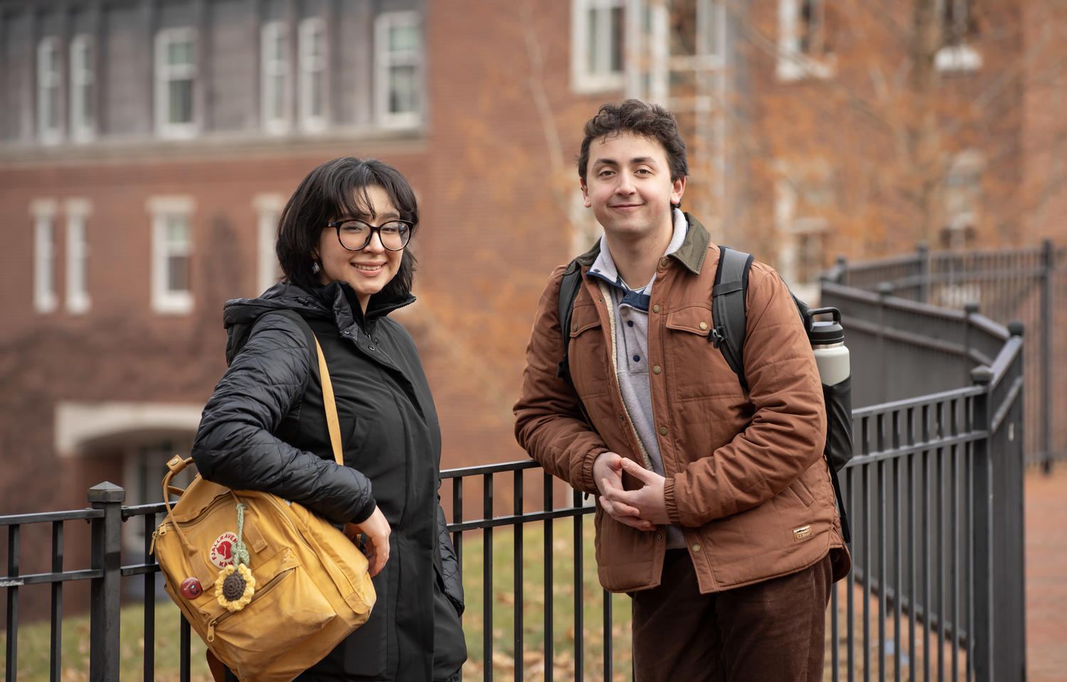 A female and a male student pose for a picture in front of a brick building.