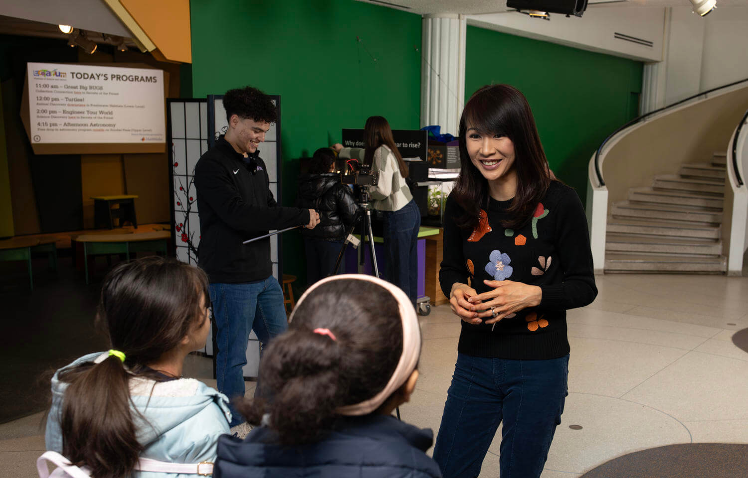 Woman speaks with children while setting up a science experiment at a museum.