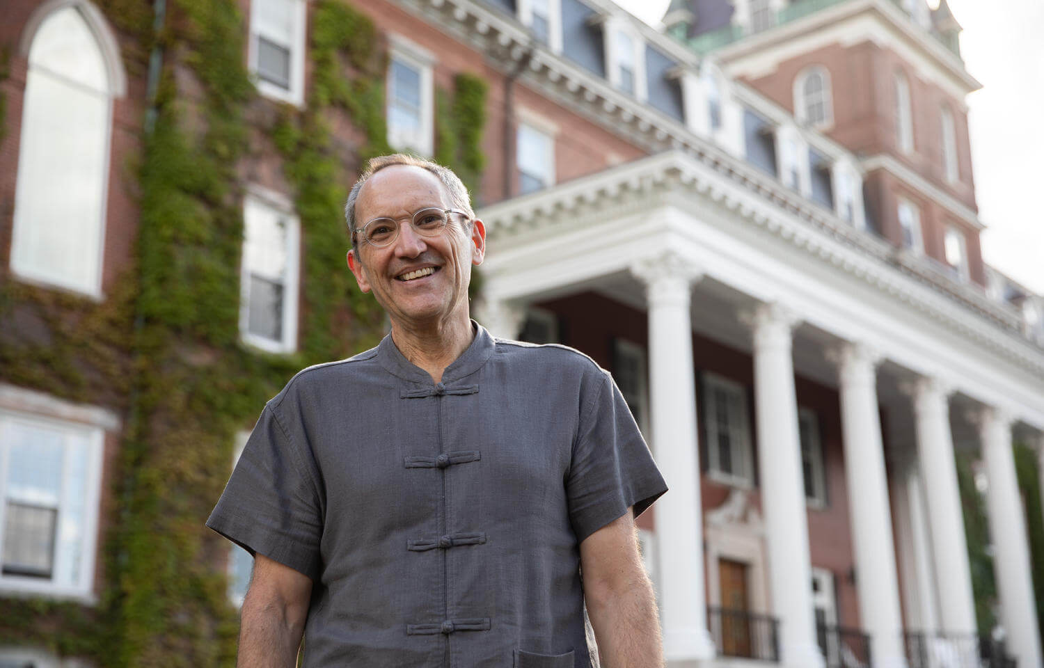 Professor stands in front of brick building with a white porch.