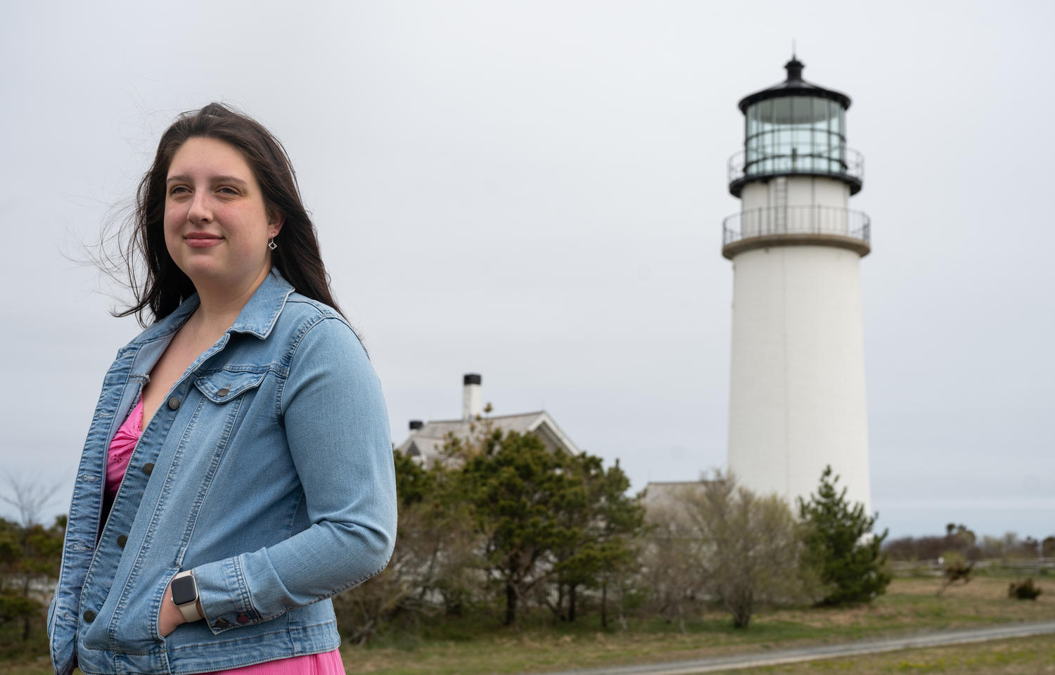 Young woman stands in front of a lighthouse on Cape Cod.