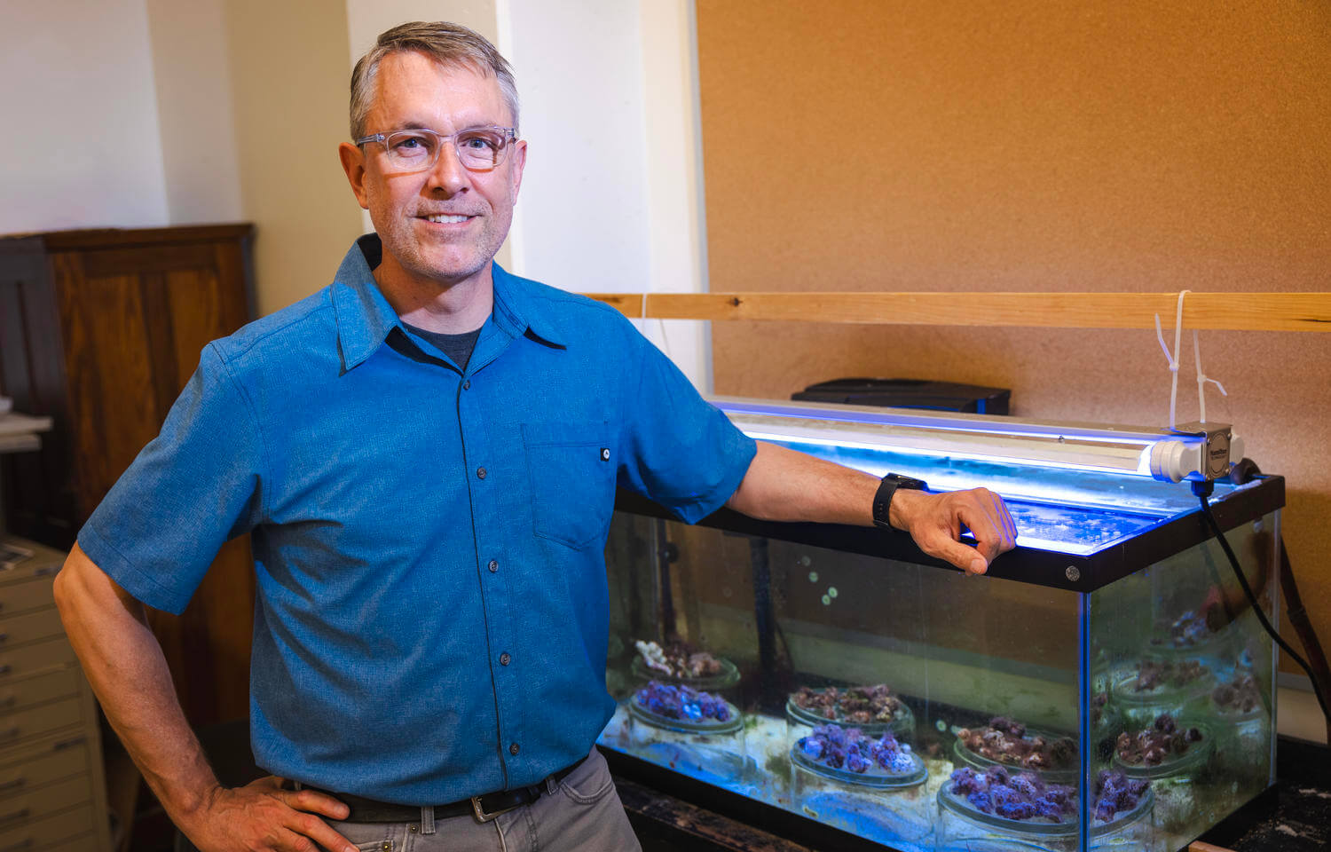 Man standing next to aquarium filled with sea coral.