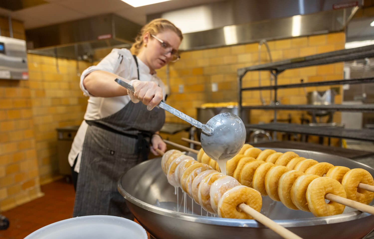 Woman ladles glaze over donuts