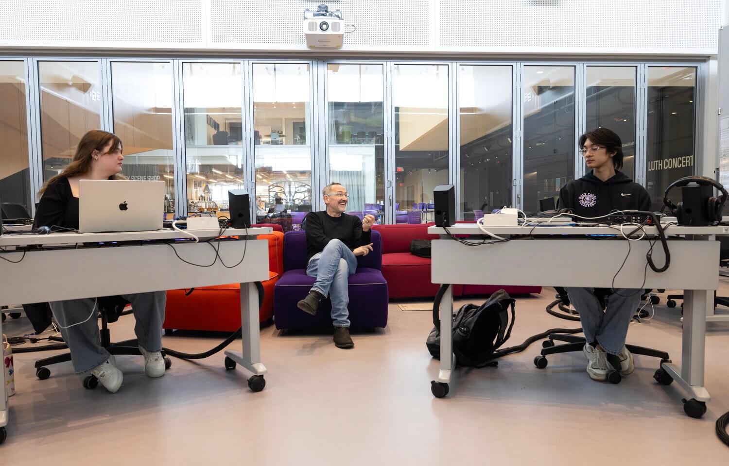 Man on couch in between two people at desks
